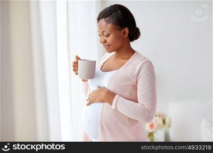 pregnancy, people and expectation concept - happy african american pregnant woman with cup drinking tea at home. happy pregnant woman with cup drinking tea at home