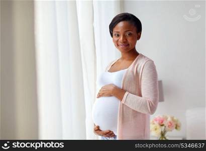 pregnancy, people and expectation concept - happy pregnant african american woman at home window. pregnant african american woman at home window