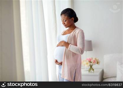 pregnancy, people and expectation concept - happy pregnant african american woman at home window. pregnant african american woman at home window