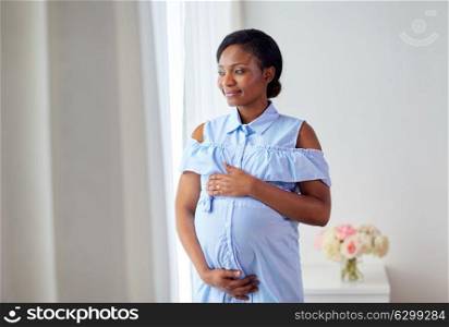 pregnancy, people and expectation concept - happy pregnant african american woman looking through window at home. pregnant woman looking through window at home