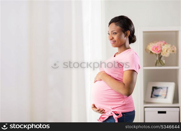 pregnancy, people and expectation concept - happy pregnant african american woman with big belly looking through window at home. happy pregnant woman with big belly at home