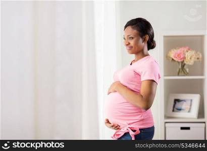 pregnancy, people and expectation concept - happy pregnant african american woman with big belly looking through window at home. happy pregnant woman with big belly at home