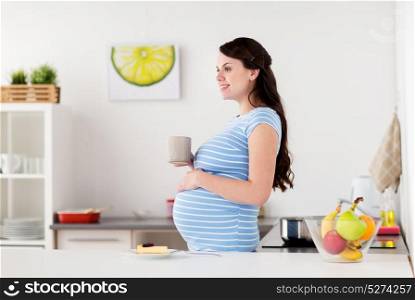 pregnancy, people and expectation concept - happy pregnant woman with cup of tea and piece of cake at home kitchen. happy pregnant woman with mug and cake at home