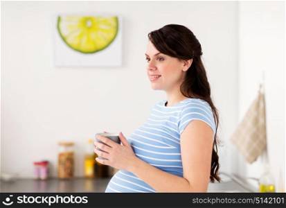 pregnancy, people and expectation concept - happy pregnant woman with cup of tea at home kitchen. happy pregnant woman with cup at home kitchen