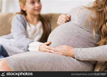 pregnancy, people and family concept - close up of pregnant woman with girl sitting on sofa and talking at home. close up of pregnant woman and girl at home