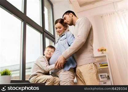 pregnancy, people and family concept - happy father and little son hugging pregnant mother at home. happy family with pregnant mother at home