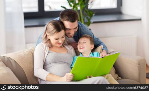 pregnancy, people and family concept - happy pregnant mother, father and little son reading book on sofa at home. happy family reading book at home