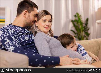 pregnancy, people and family concept - happy pregnant mother, father and little son hugging on sofa at home. happy family with pregnant mother at home