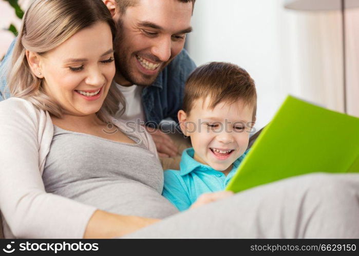 pregnancy, people and family concept - happy pregnant mother, father and little son reading book on sofa at home. happy family reading book at home