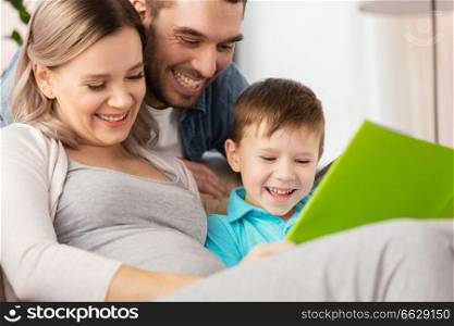 pregnancy, people and family concept - happy pregnant mother, father and little son reading book on sofa at home. happy family reading book at home