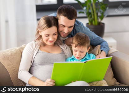 pregnancy, people and family concept - happy pregnant mother, father and little son reading book on sofa at home. happy family reading book at home