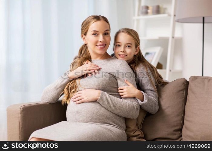 pregnancy, people and family concept - happy pregnant woman with girl sitting on sofa and talking and hugging at home. happy pregnant woman and girl hugging at home