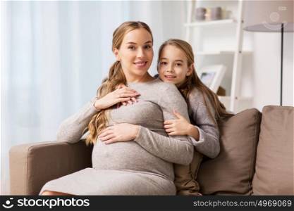 pregnancy, people and family concept - happy pregnant woman with girl sitting on sofa and talking and hugging at home. happy pregnant woman and girl hugging at home