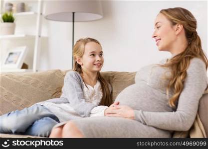 pregnancy, people and family concept - happy pregnant woman with girl sitting on sofa and talking at home. happy pregnant woman and girl on sofa at home