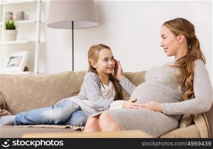 pregnancy, people and family concept - happy pregnant woman with girl sitting on sofa and talking at home. happy pregnant woman and girl on sofa at home