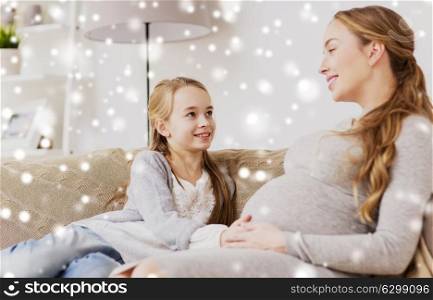pregnancy, people and family concept - happy pregnant woman with girl sitting on sofa and talking at home over snow. happy pregnant woman and girl on sofa at home