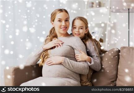 pregnancy, people and family concept - happy pregnant woman with girl sitting on sofa and talking and hugging at home over snow. happy pregnant woman and girl hugging at home