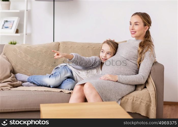 pregnancy, people and family concept - happy pregnant woman with girl sitting on sofa at home. happy pregnant woman and girl on sofa at home