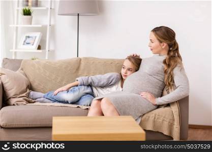 pregnancy, people and family concept - happy pregnant woman with girl sitting on sofa at home. happy pregnant woman and girl on sofa at home