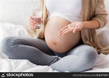 pregnancy, people and health care concept - close up of pregnant woman sitting in bed at home with pills and glass of water. close up of pregnant woman with pills in bed