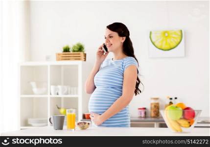 pregnancy, people and healthy eating concept - happy pregnant woman calling on smartphone and having breakfast at home kitchen. happy pregnant woman calling on smartphone at home