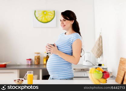pregnancy, people and healthy eating concept - happy pregnant woman with cup of tea and food having breakfast at home kitchen. happy pregnant woman with cup at home kitchen