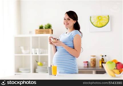 pregnancy, people and healthy eating concept - happy pregnant woman with muesli for breakfast at home kitchen. pregnant woman eating muesli for breakfast at home