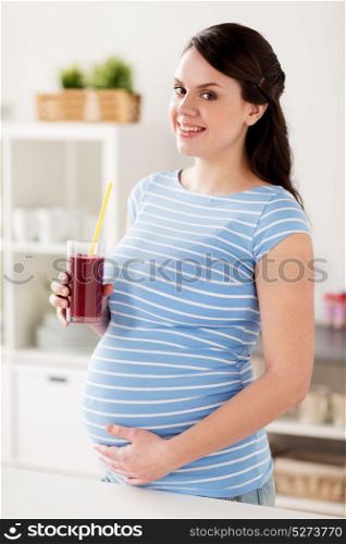 pregnancy, people and healthy eating concept - happy smiling pregnant woman drinking juice or smoothie at home kitchen. happy pregnant woman drinking juice at home