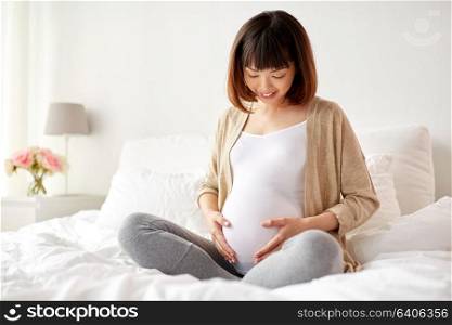 pregnancy, people and maternity concept - happy pregnant asian woman sitting in bed at home bedroom. happy pregnant asian woman sitting in bed at home
