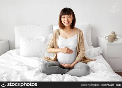 pregnancy, people and maternity concept - happy pregnant asian woman sitting in bed at home bedroom. happy pregnant asian woman sitting in bed at home. happy pregnant asian woman sitting in bed at home