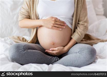 pregnancy, people and maternity concept - pregnant woman sitting in bed at home and touching bare belly. pregnant woman with bare belly sitting in bed