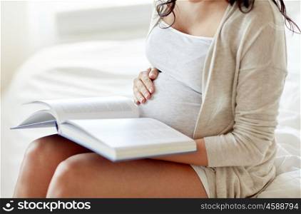 pregnancy, people and motherhood concept - close up of pregnant woman reading book sitting on bed at home bedroom