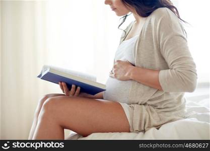 pregnancy, people and motherhood concept - close up of pregnant woman reading book sitting on bed at home bedroom