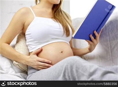 pregnancy, people and motherhood concept - close up of pregnant woman sitting on sofa and reading book