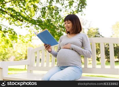 pregnancy, people and motherhood concept - happy pregnant asian woman sitting on park bench and reading book. happy pregnant asian woman reading book at park