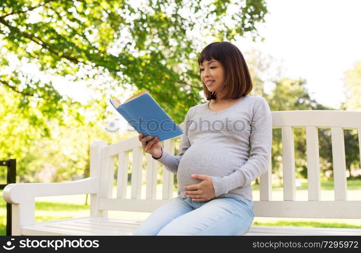 pregnancy, people and motherhood concept - happy pregnant asian woman sitting on park bench and reading book. happy pregnant asian woman reading book at park