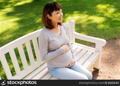 pregnancy, people and motherhood concept - happy pregnant asian woman sitting on park bench. happy pregnant asian woman sitting on park bench
