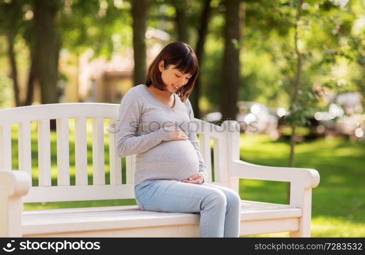 pregnancy, people and motherhood concept - happy pregnant asian woman sitting on park bench. happy pregnant asian woman sitting on park bench
