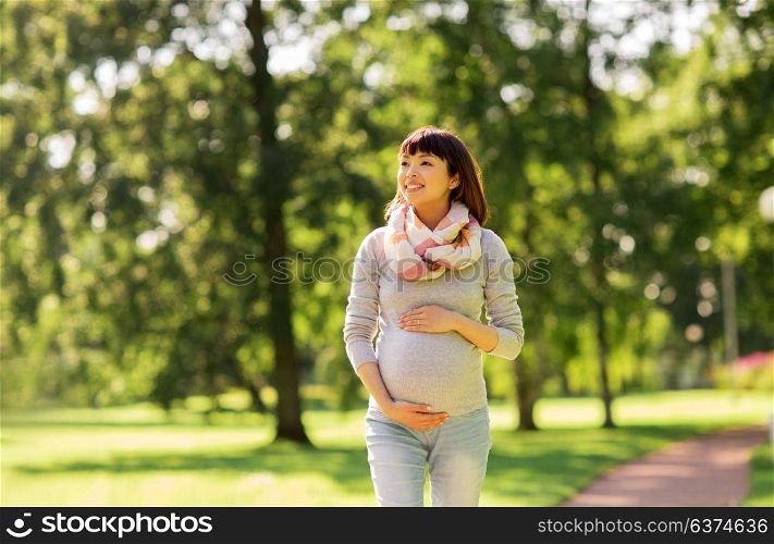 pregnancy, people and motherhood concept - happy pregnant asian woman walking at park. happy pregnant asian woman walking at park