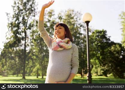 pregnancy, people and motherhood concept - happy pregnant asian woman waving hand at park. happy pregnant asian woman waving hand at park