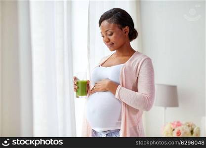 pregnancy, people and rest concept - happy pregnant african american woman drinking green vegetable juice or smoothie at home. pregnant woman drinking vegetable juice at home