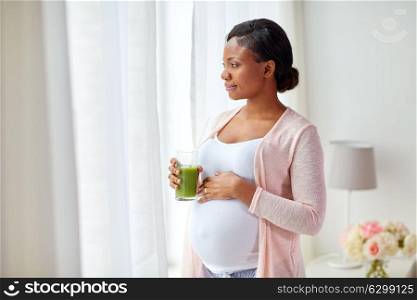 pregnancy, people and rest concept - happy pregnant african american woman drinking green vegetable juice or smoothie at home. pregnant woman drinking vegetable juice at home