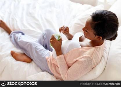 pregnancy, people and rest concept - happy pregnant african american woman drinking green vegetable juice or smoothie in bed at home. pregnant woman drinking vegetable juice in bed