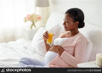 pregnancy, people and rest concept - happy pregnant african american woman drinking orange juice in bed at home. pregnant woman drinking orange juice in bed