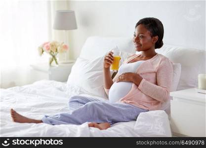 pregnancy, people and rest concept - happy pregnant african american woman drinking orange juice in bed at home. pregnant woman drinking orange juice in bed. pregnant woman drinking orange juice in bed