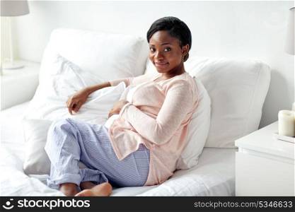 pregnancy, people and rest concept - happy pregnant african american woman lying in bed at home bedroom. happy pregnant african woman lying in bed at home