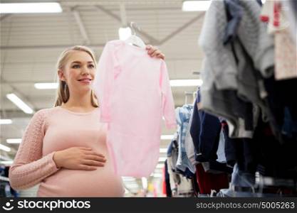 pregnancy, people and shopping concept - happy pregnant woman with pink baby bodysuit at clothing store. pregnant woman with baby clothes at clothing store