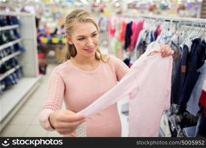 pregnancy, people and shopping concept - happy pregnant woman with pink baby bodysuit at clothing store. pregnant woman with baby clothes at clothing store