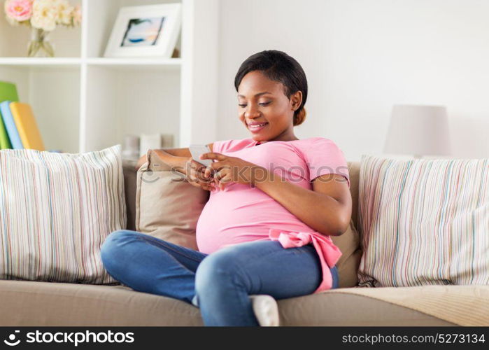 pregnancy, people and technology concept - happy pregnant african american woman with smartphone at home. happy pregnant woman with smartphone at home