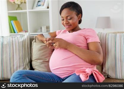 pregnancy, people and technology concept - happy pregnant african american woman with smartphone at home. happy pregnant woman with smartphone at home
